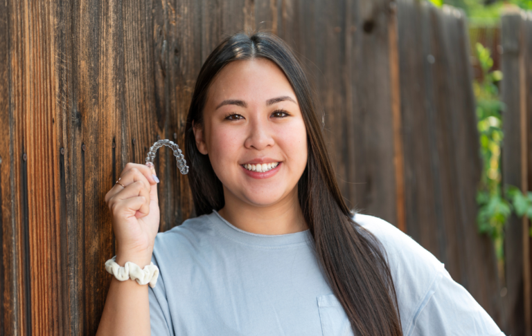 Girl with brown hair smiling holding Invisalign aligner trays.